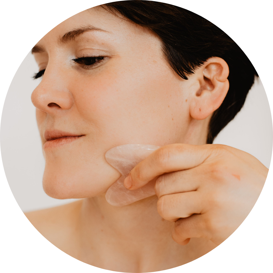 Woman with short hair practicing facial gua sha with a rose quartz gua sha stone.