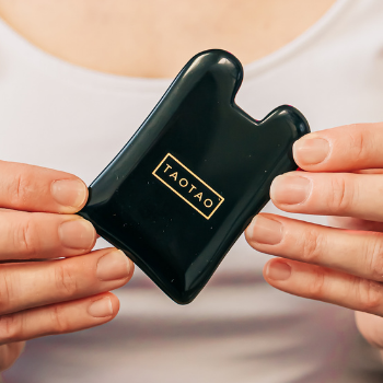 Person holding an obsidian gua sha stone with the logo "Tao Tao" in gold, created by local business owner Amy Tao of Based Wellness.
